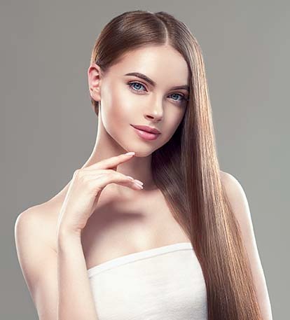 A young woman with long, straight hair poses gracefully against a neutral background. She has striking blue eyes and a soft, natural makeup look. Her hand is gently placed near her face, and she appears confident and serene. The lighting highlights her smooth skin and the shine of her hair.